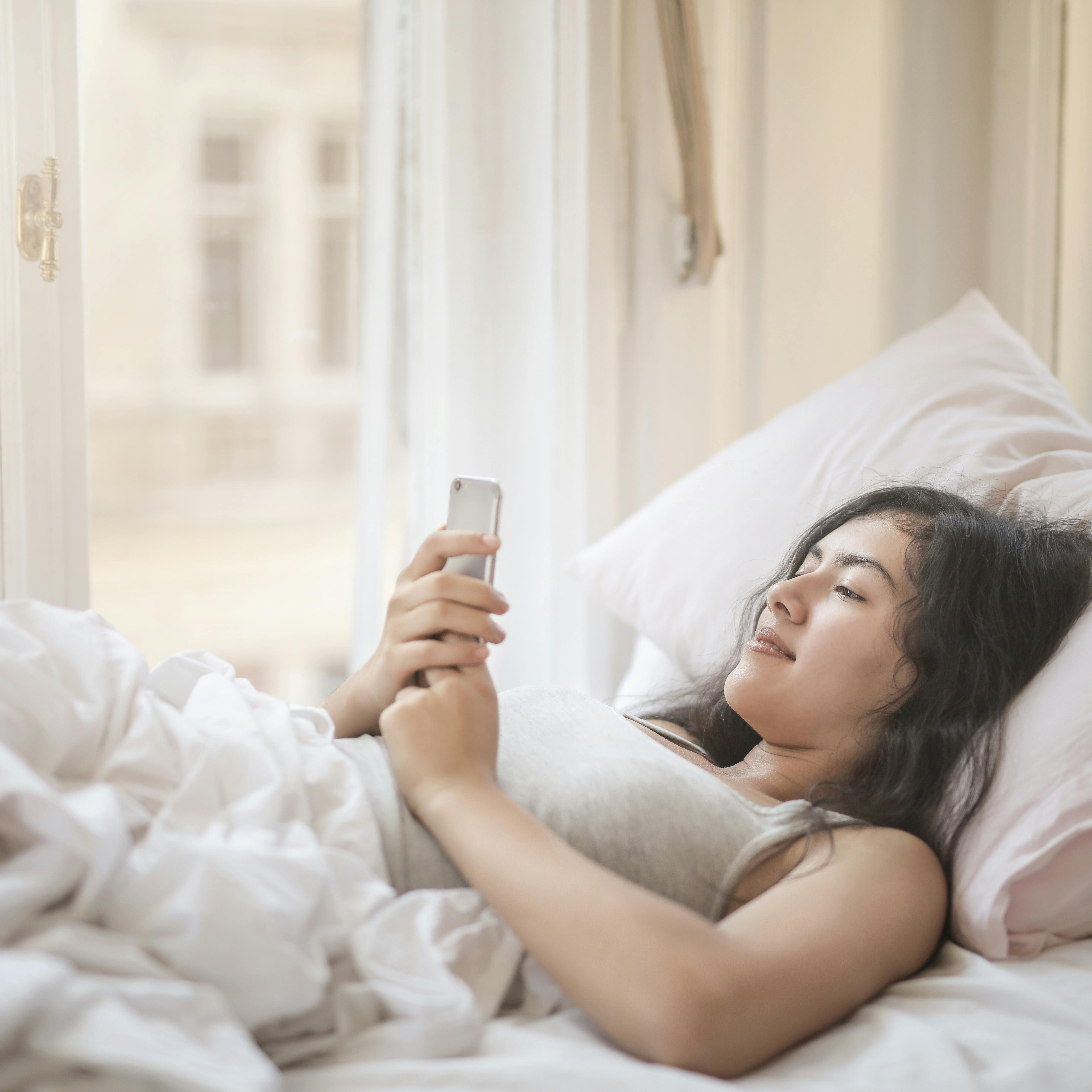 ベッドでスマホを見る女性の画像